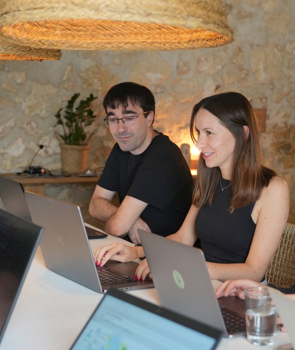 Zwei Teammitglieder einer Digitalagentur arbeiten lächelnd gemeinsam an Laptops in einem modernen Büro mit gemütlicher Atmosphäre.